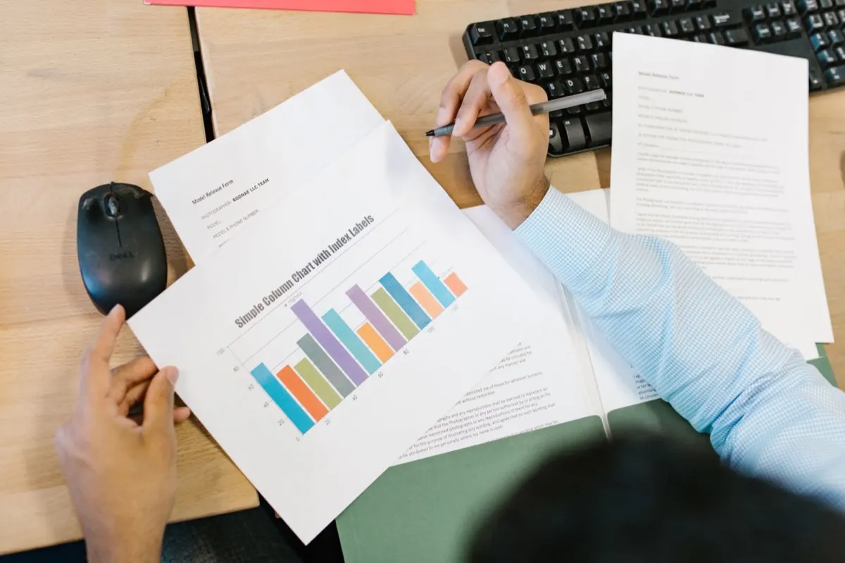 A person with a pen checking printed report pages with a column chart