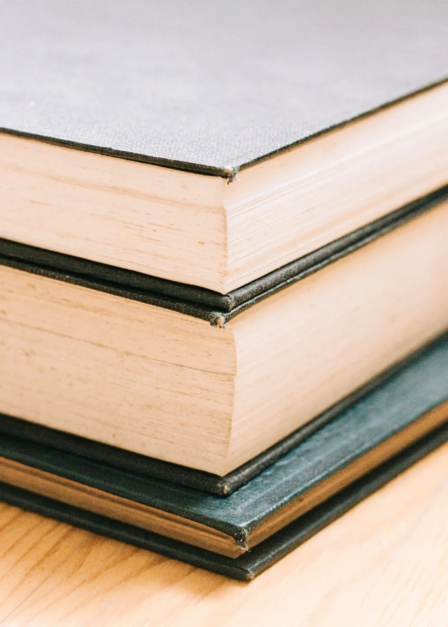 A stack of hard-bound volumes with cloth covers, showing the rigid boards around the pages